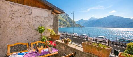 A balcony with a table set for dining, overlooking a body of water and mountains.