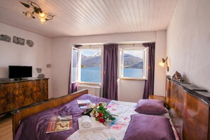 A bedroom with a bed, a dresser, a television, and a window with a view of mountains and water. - Nobiallo Fantastico (Menaggio)
