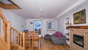 A spacious living area with a wooden staircase, a dining table with chairs, a gray sofa, a fireplace, and a painting on the wall. - Nobiallo Fantastico (Menaggio)