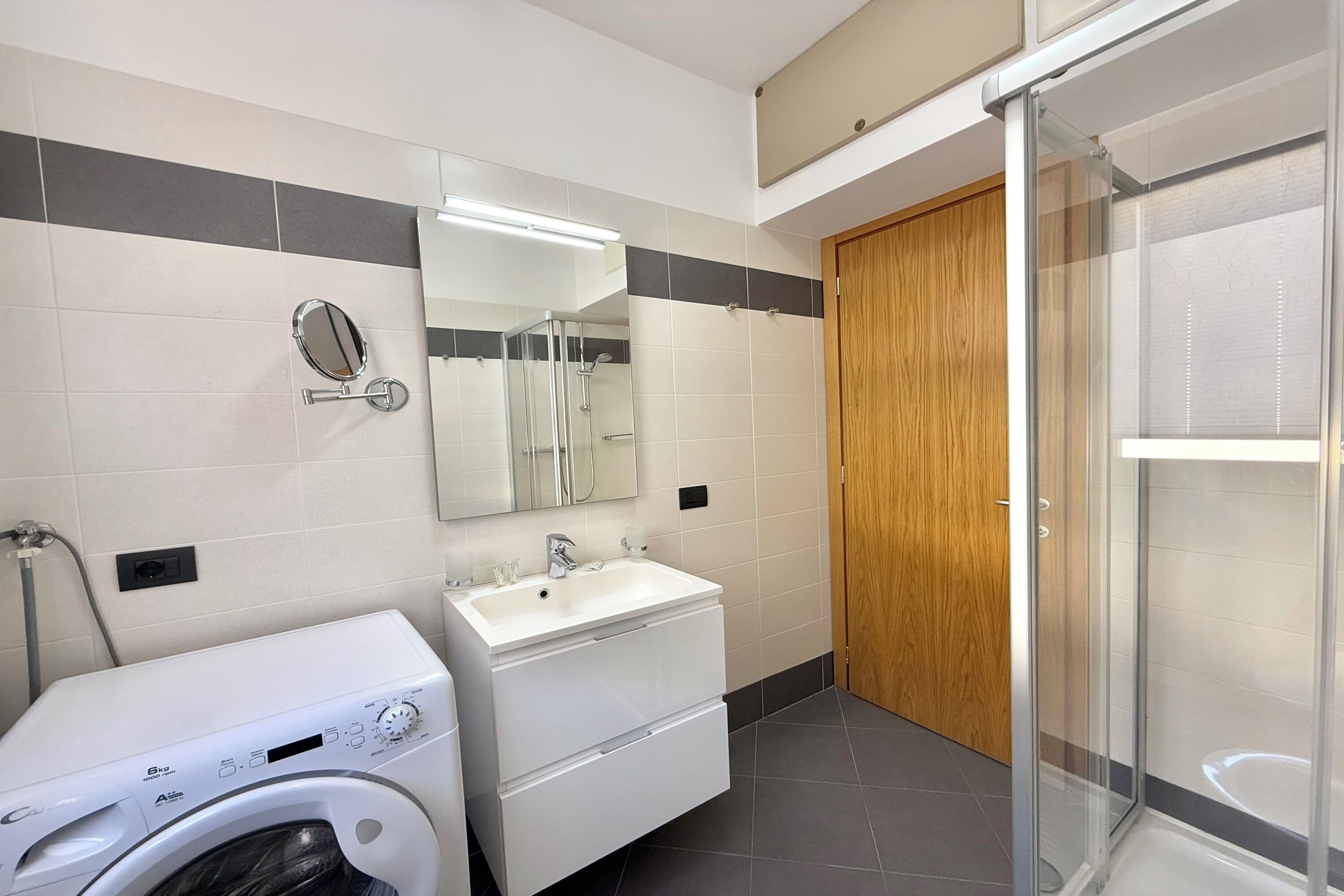 Un bagno moderno dotato di lavatrice, lavandino e zona doccia.