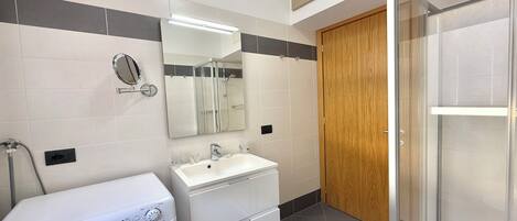 Un bagno moderno dotato di lavatrice, lavandino e zona doccia.