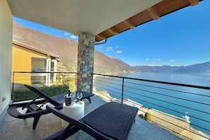 A balcony with wicker furniture, a stone pillar, and a view of a lake and mountains.