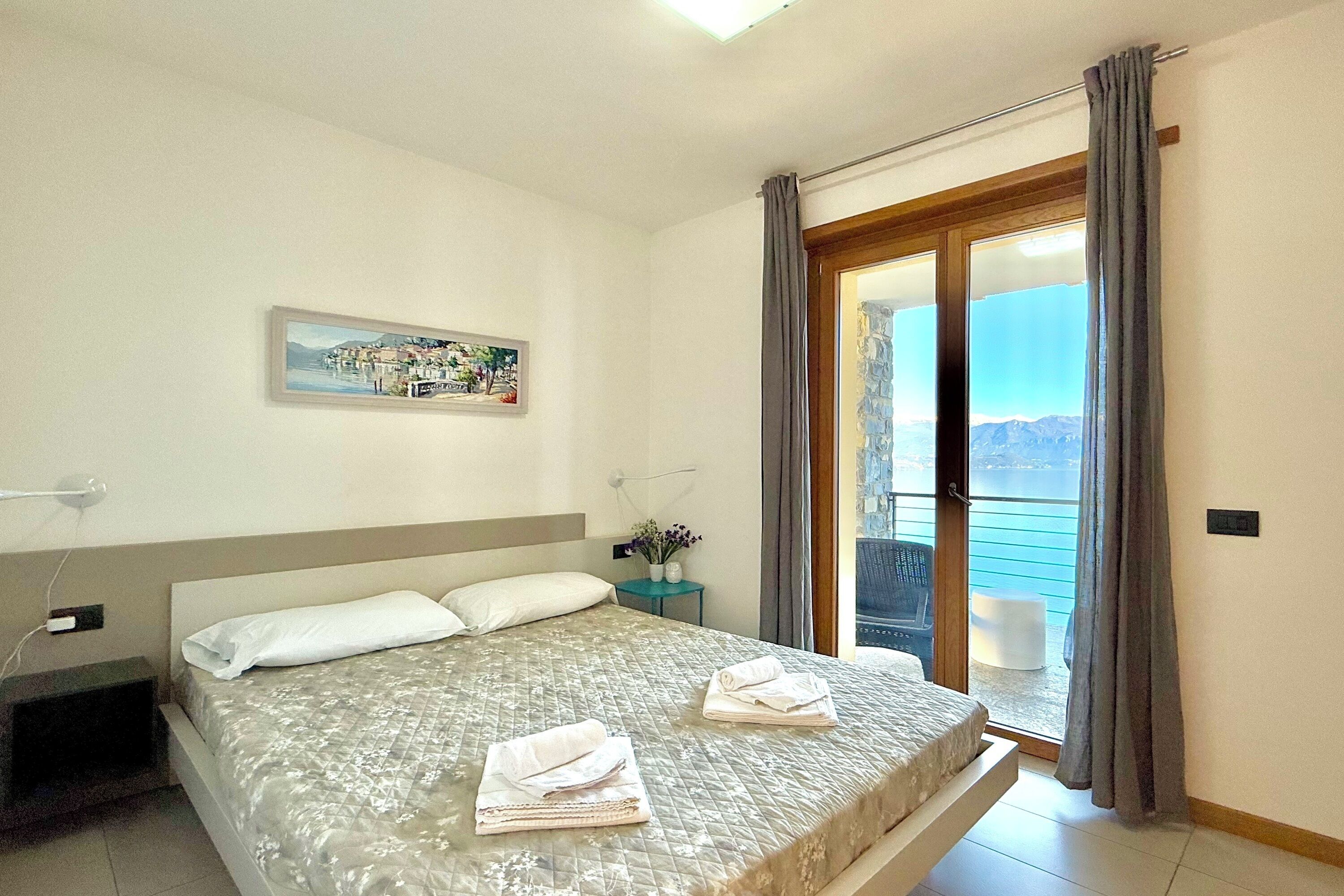 A bedroom with a bed, a nightstand, a painting, and a view of the outdoors through a sliding door.