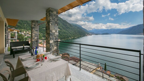 A dining area with a table set for two, overlooking a lake with mountains in the background. - Residence degli Oleandri 5A (Argegno)
