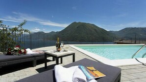 A poolside area with lounge chairs, a table with a bottle and glasses, and a view of mountains. - Residence degli Oleandri 5A (Argegno)