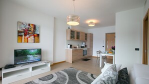A modern living room with a flat-screen TV, a sofa, a coffee table, and a kitchen area with cabinets and a microwave. - Residence degli Oleandri 5A (Argegno)