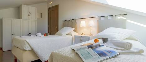 Un dormitorio con dos camas, un tragaluz, una mesita de noche con lámparas y una revista sobre la cama.