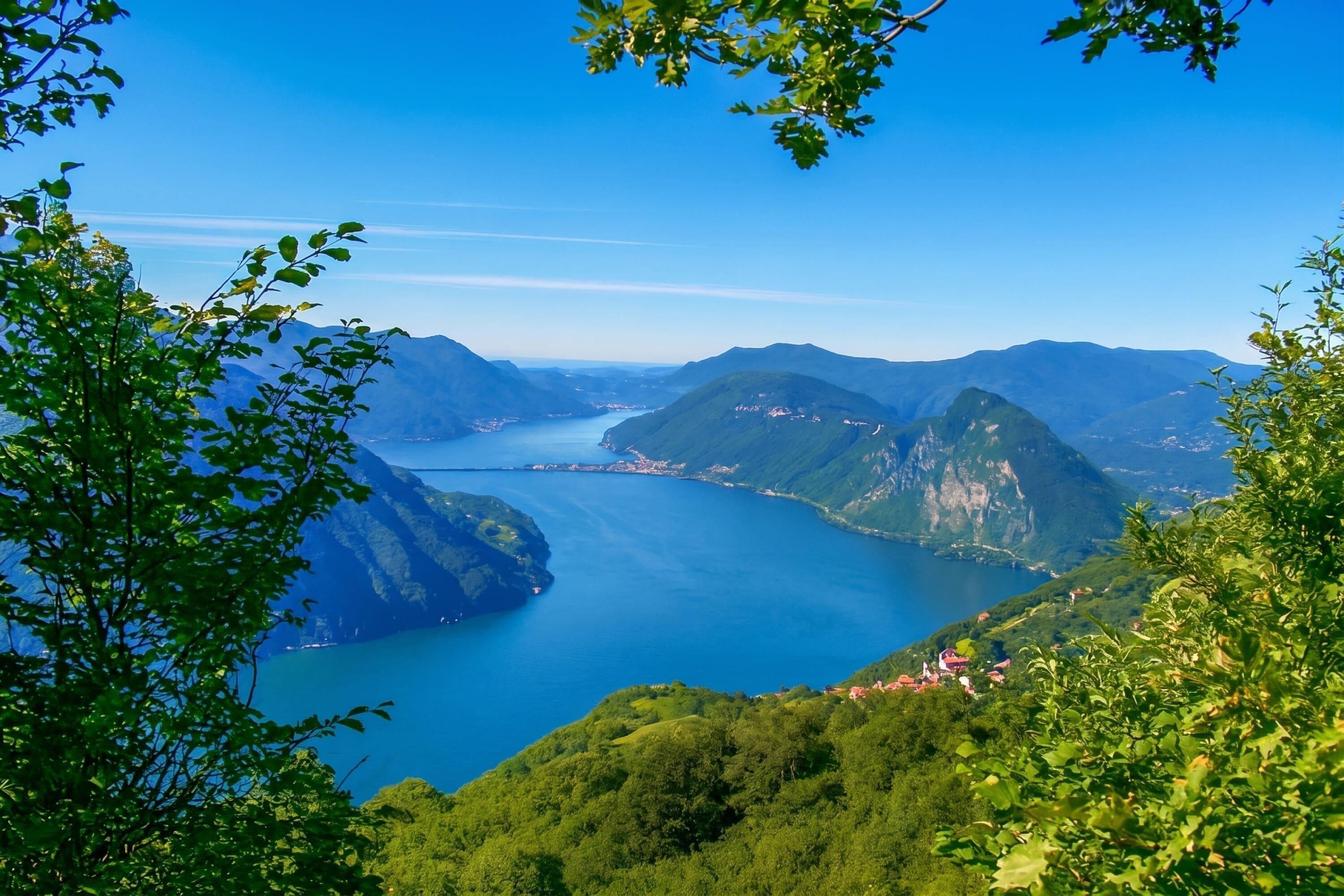 Un paysage montagneux avec un lac, entouré de verdure et de bâtiments situés au loin.