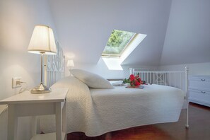 A bedroom with a skylight, a bedside table with a lamp, a bed with a white comforter, and a dresser. - Casa Al Prato Apt. F (Varenna)