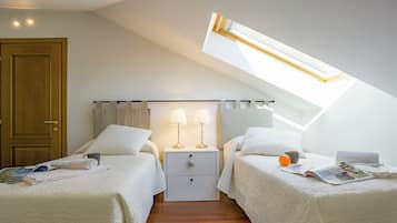 Une chambre avec deux lits, une porte en bois, une table de chevet avec des lampes et une lucarne.