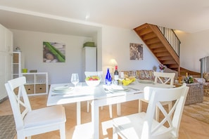 A dining area with a white table set for four, a staircase, and a kitchen area in the background. - Casa Al Prato Apt. F (Varenna)