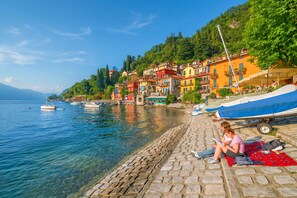 A waterfront scene with boats, a cobblestone path, and colorful buildings. - Casa Al Prato Apt. F (Varenna)