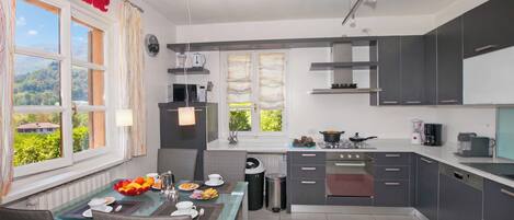 Una cocina moderna con armarios grises, un comedor con mesa de vidrio y vistas a zonas verdes.