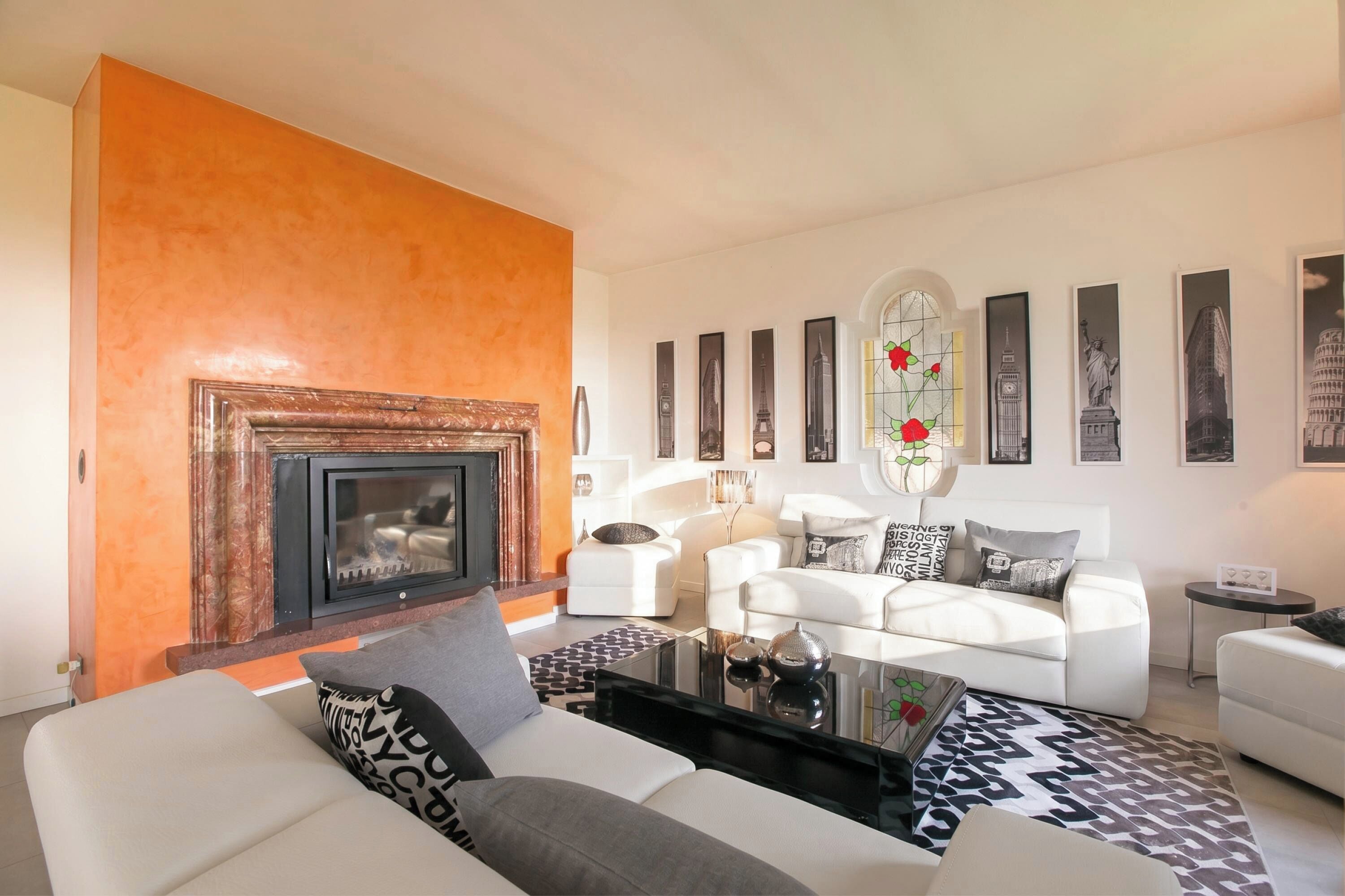A living room with a fireplace, white sofas, a coffee table, and a wall with framed pictures.