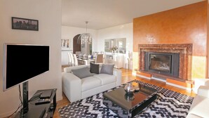 Una sala de estar moderna con televisor de pantalla plana, un sofá, una chimenea y un comedor al fondo.