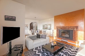 A modern living room with a flat-screen TV, a sofa, a fireplace, and a dining area in the background. - Villa Lakecomo - Ritrovo (Menaggio)