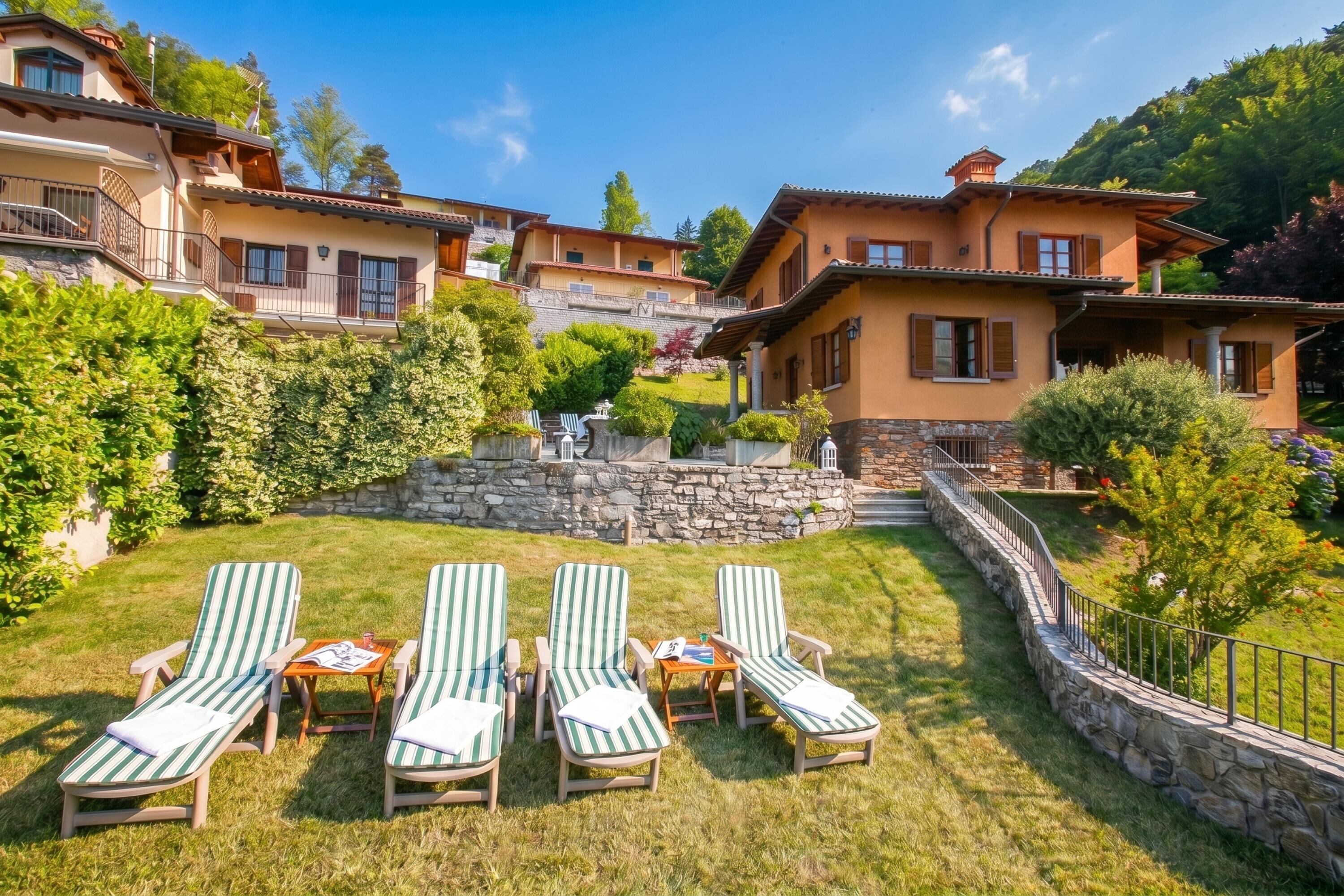 A hillside villa with a stone retaining wall, a grassy lawn, and three lounge chairs.
