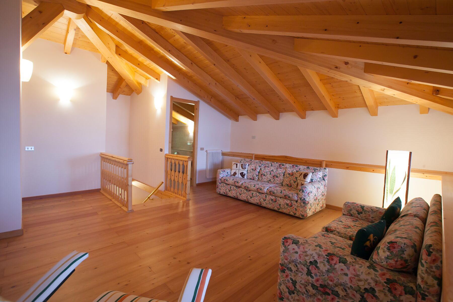 A spacious loft with wooden beams, a floral sofa, and a wooden staircase.