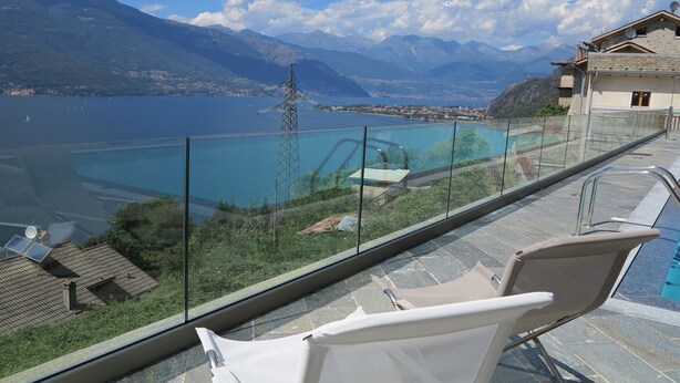 A balcony with a glass railing overlooking a pool and a mountainous landscape. - Riva Bellano Camelia 1 (Bellano)