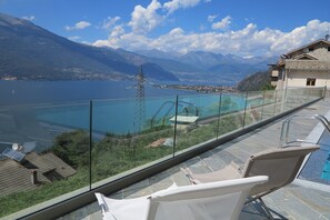 A balcony with a glass railing overlooking a pool and a mountainous landscape.