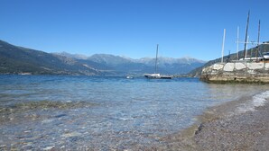 A clear lake with a sailboat anchored near a rocky shore. Mountains are visible in the background. - Riva Bellano Camelia 1 (Bellano)