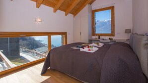 A bedroom with a large bed, a wooden ceiling, a window with a mountain view, and a balcony. - Riva Bellano Camelia 1 (Bellano)