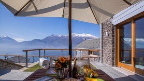 A terrace with a table set for dining, a bottle of champagne, and a view of snow-capped mountains. - Riva Bellano Camelia 1 (Bellano)