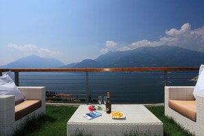 A balcony with wicker furniture, a table with a bottle, glasses, a rose, and a plate of snacks.