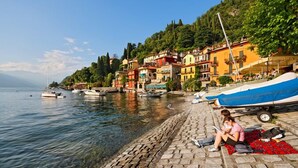 A waterfront scene with colorful buildings, boats, and a cobblestone path. - Riva Bellano Orchidea 3 (Bellano)