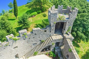 A stone castle with a central tower, surrounded by lush greenery and a clear sky.