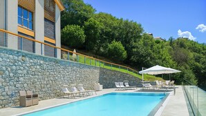 A swimming pool with lounge chairs and umbrellas, surrounded by a stone wall and a glass railing. - Riva Bellano Margherita 2 (Bellano)