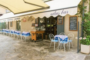 Un espacio al aire libre con mesas y sillas, un panel de menú y la entrada a un bar.