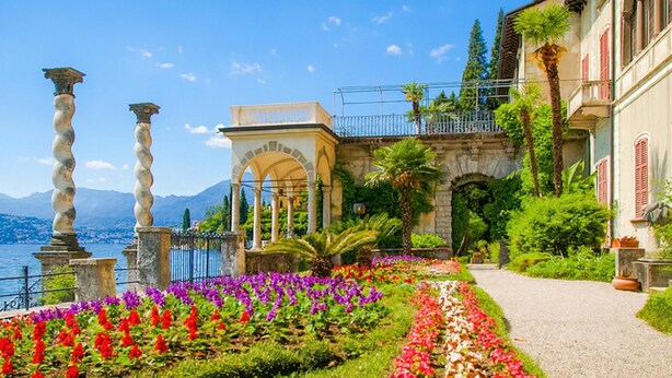 A garden with a pathway, a building with columns, and a view of the water. - Riva Bellano Margherita 2 (Bellano)