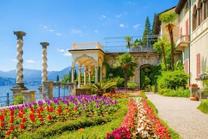 Un jardin avec un sentier, un bâtiment doté de colonnes et une vue sur l’eau.