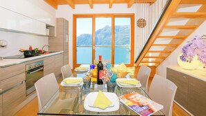A modern kitchen with a dining area, wooden ceiling, large windows with a mountain view, and a staircase. - Riva Bellano Margherita 2 (Bellano)
