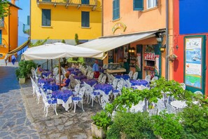 Outdoor seating with white chairs and tables, a pizza shop, and a sign for 'VIA BOAT'. - Riva Bellano Margherita 2 (Bellano)