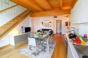 A modern kitchen with a dining area, wooden ceiling beams, and a staircase. - Riva Bellano Margherita 2 (Bellano)