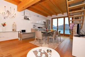 Une cuisine moderne avec des meubles blancs, un coin repas doté d’une table en verre et une vue sur un lac, visible à travers de grandes fenêtres.