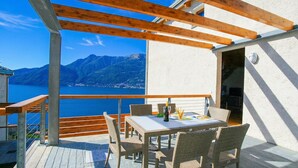An outdoor patio with a table and chairs, a wooden pergola, and a view of mountains and water. - Riva Bellano Margherita 2 (Bellano)