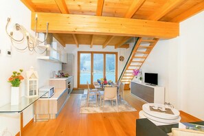 A modern kitchen with wooden beams, a dining area with a table and chairs, a TV, and a view of the sea through large windows. - Riva Bellano Margherita 2 (Bellano)