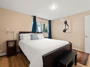 A bedroom with a bed, bedside tables, a bench, a window with curtains, and a wall-mounted artwork.