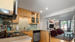 A modern kitchen with wooden cabinets, a dishwasher, and a dining area with a red chair and a table. - 2-BR Condo by Vail Resort: Outdoor Patio, Parking (Vail)