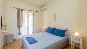 Un dormitorio con cama, mesita de noche con lámpara, ventana con cortinas y aire acondicionado de pared.