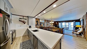 A modern kitchen with a large island, stainless steel appliances, and a dining area with a wooden table and chairs. - Slopeside 1849 Condos - Comfortable 3 BR Condos with Full Kitchens (Mammoth Lakes)