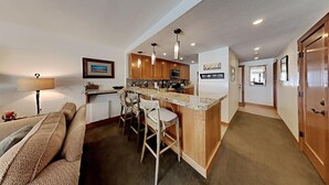 A compact kitchen with a central island, bar stools, wooden cabinets, and a microwave. - Renovated Condo Across the Street from Mountain Biking Trails! by RedAwning (Mammoth Lakes)