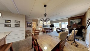 A spacious living room with a wooden dining table, chairs, a sofa, and a fireplace. There are framed pictures on the walls and a chandelier hanging from the ceiling. - 2 Bedroom Condo Just Steps Away From Summer Recreational Activities by RedAwning (Mammoth Lakes)