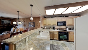 A modern kitchen with granite countertops, wooden cabinets, a built-in microwave, and a large island with a sink. - 2 Bedroom Condo Just Steps Away From Summer Recreational Activities by RedAwning (Mammoth Lakes)