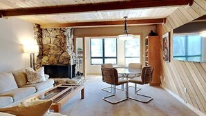 Ein gemütliches Wohnzimmer mit Kamin aus Stein, Holzboden und einem Essbereich mit Tisch und Stühlen.