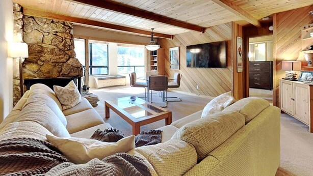 Ein gemütliches Wohnzimmer mit Kamin aus Stein, Holzboden und einem großen Fernseher an der Wand.