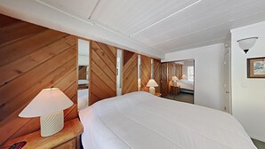A bedroom with a wooden slat wall, a bed with white bedding, two bedside lamps, and a door with a framed picture.